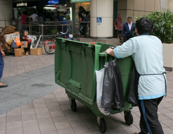 A cleaner pushing a rubbish bin